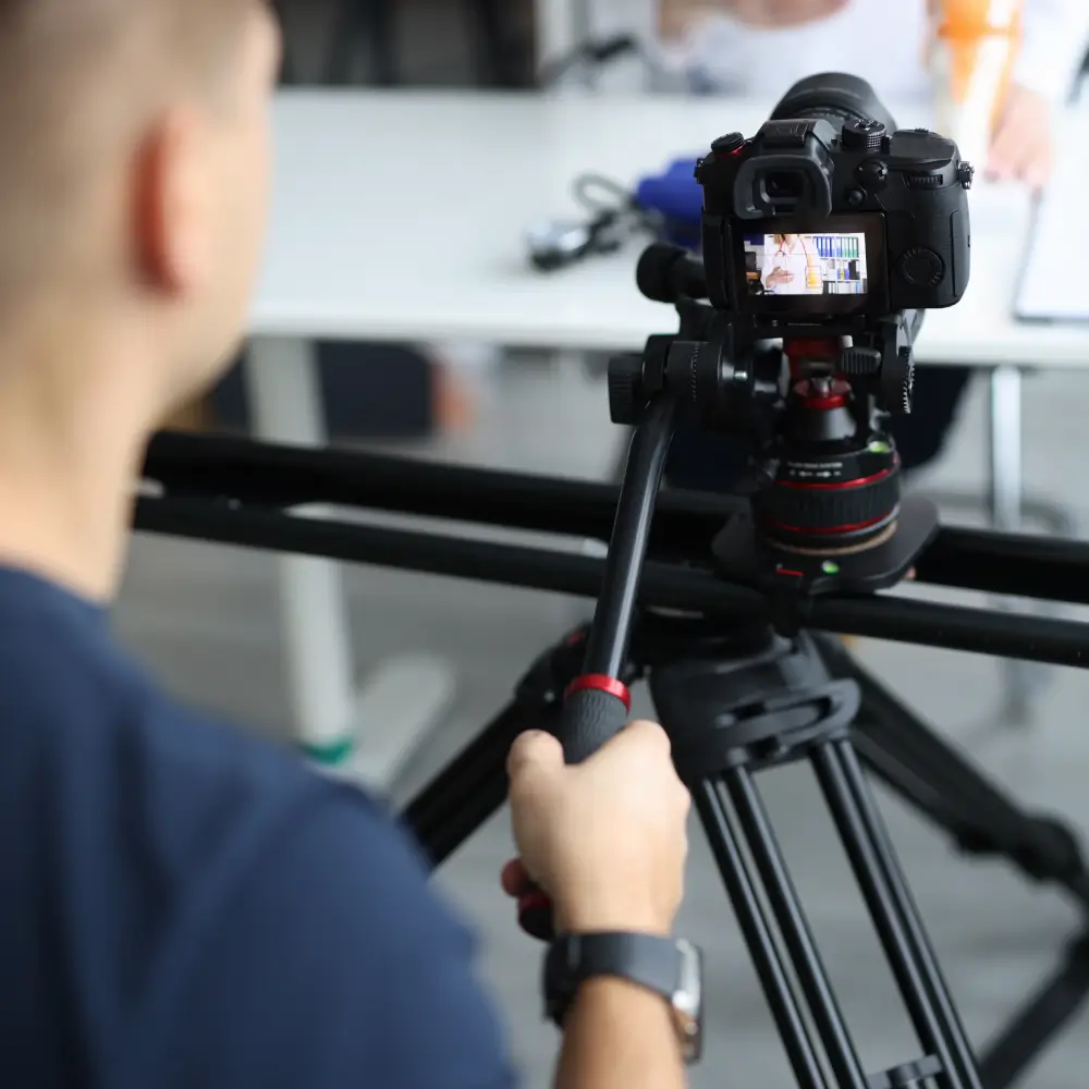 Person filming a video with a DSLR camera on a tripod slider.
