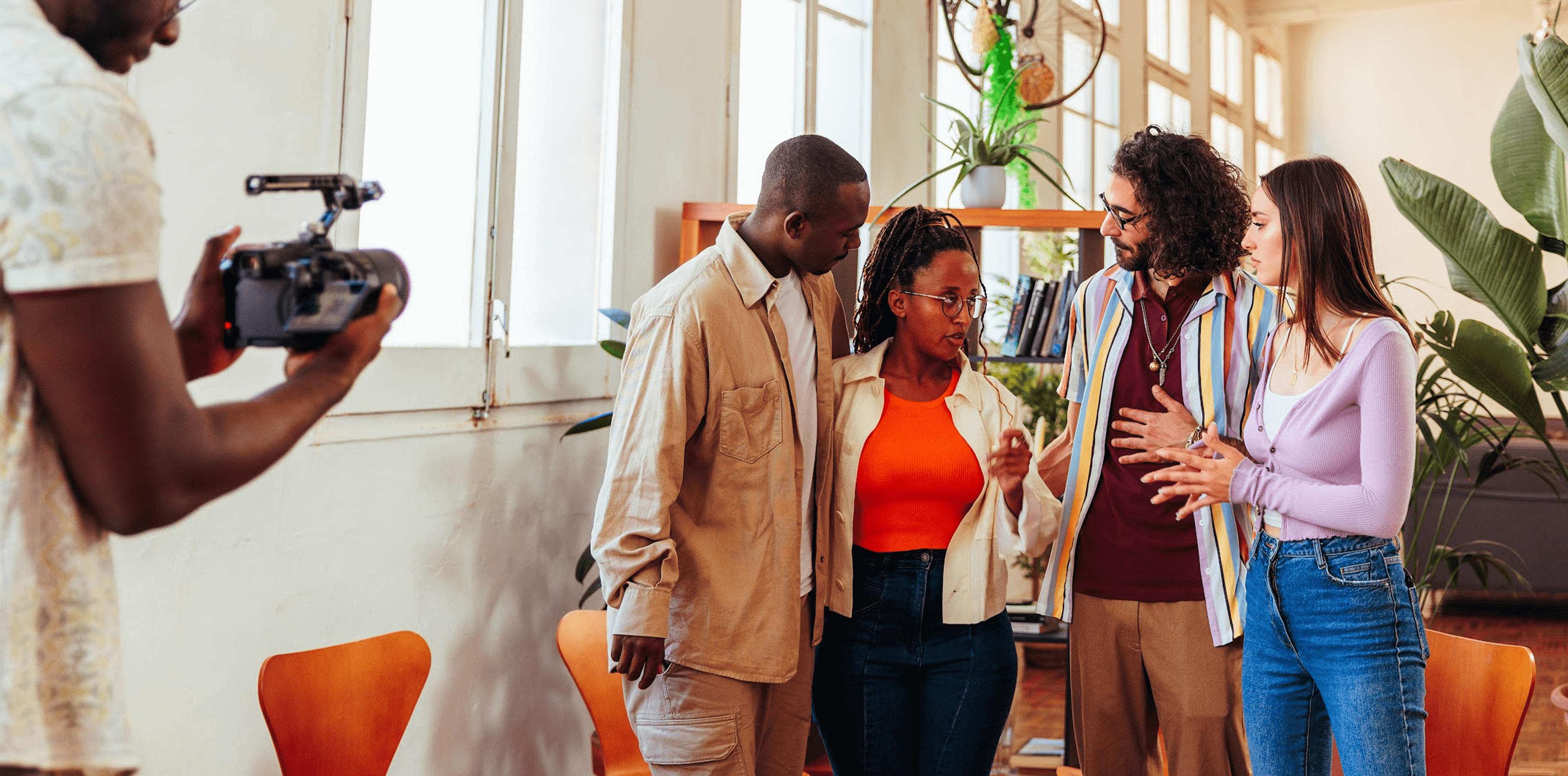 Three people conversing in a bright room with large windows.