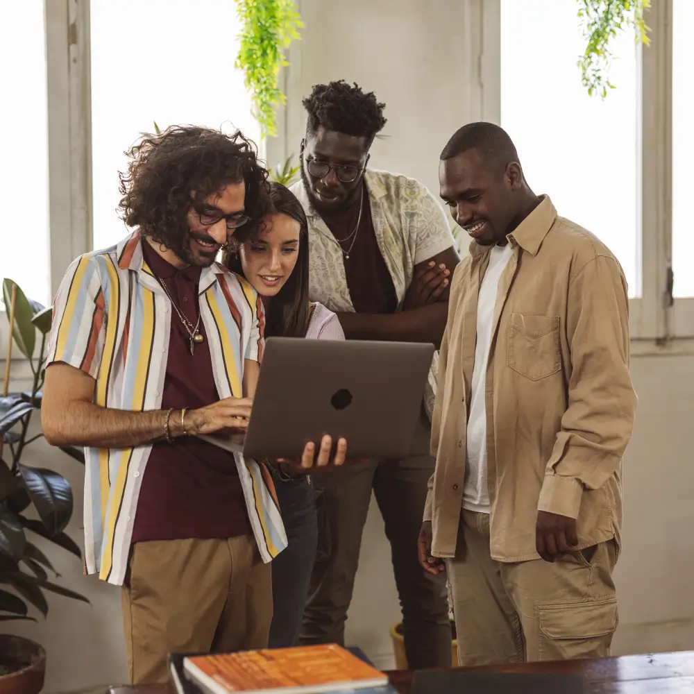 Three men looking at a laptop together in a bright office.