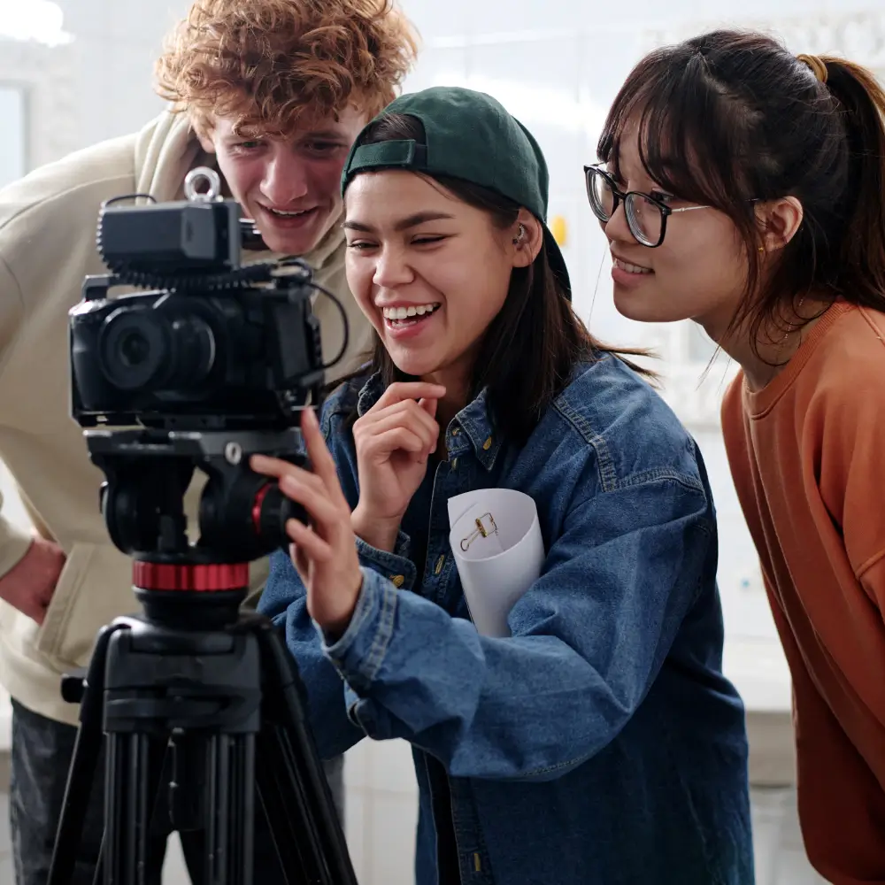 Three young adults reviewing footage on a camera screen.
