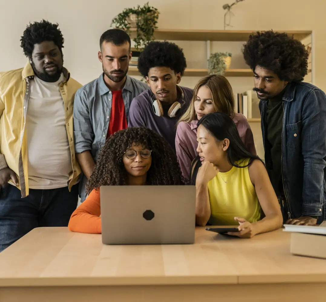 A diverse group of people gathered around a laptop.