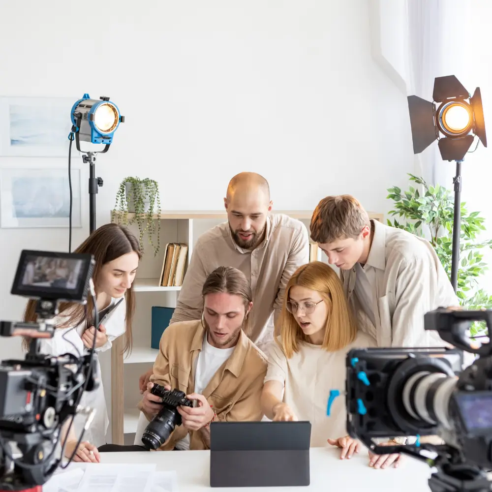 A group of five people reviewing footage on a camera in a bright studio.