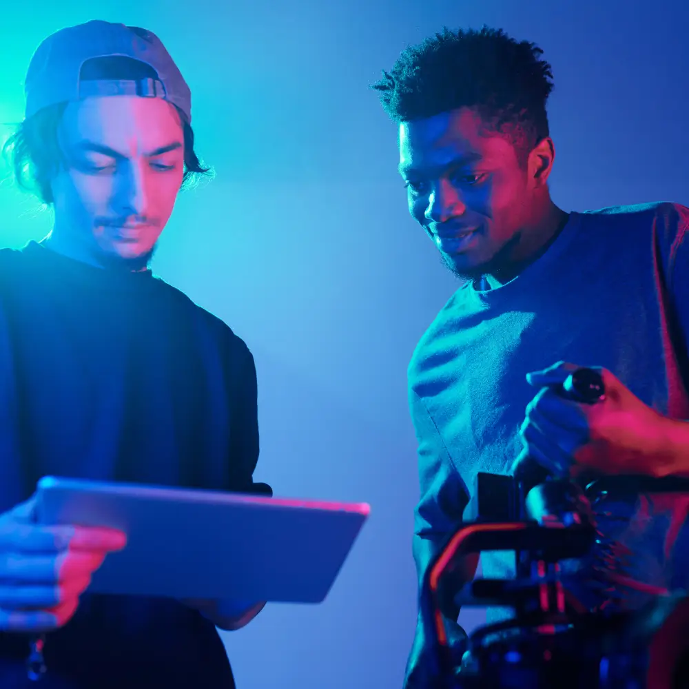 Two men working with a tablet and camera under blue lighting.